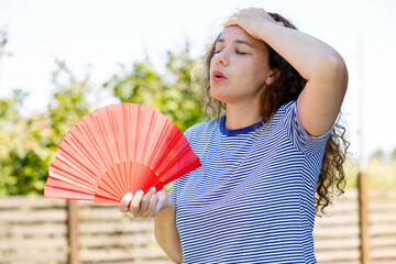 Young woman using handfan at park in a warm summer day