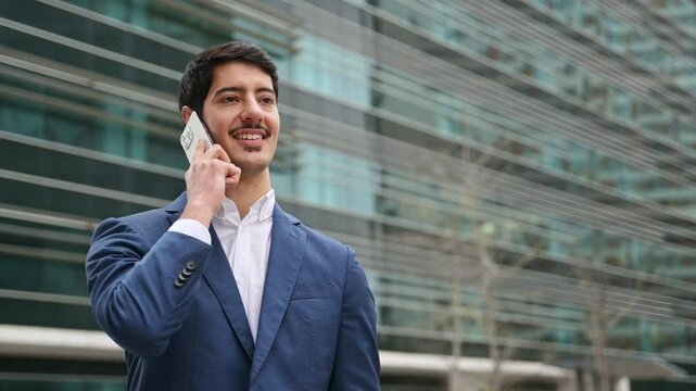 Hispanic businessman mid-conversation on his phone, the focused expression and modern city backdrop reflecting his active role in the fast-paced business world.