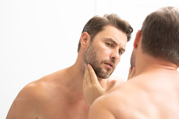 sexy man with stubble looks at the wrinkles on his face. Close up man looking in mirror, sensitive skin, cosmetology treatment. Skin care. joyful, virile, manly, attractive, naked, unshaven, handsome