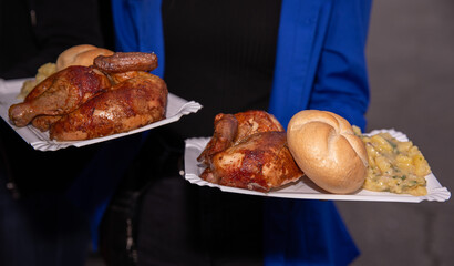 Delicious barbecue chicken, mashed potatoes, buns held on plates in hands, outdoor meal setting, comfort food concept