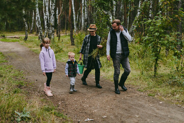 Obraz premium Happy family on a walk in the forest picking berries and herbs, traveling along paths and stones mom dad and children