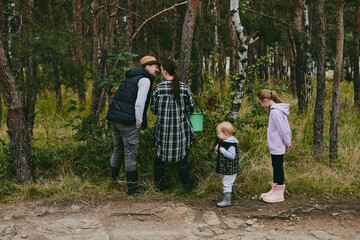 Fototapeta premium Happy family on a walk in the forest picking berries and herbs, traveling along paths and stones mom dad and children