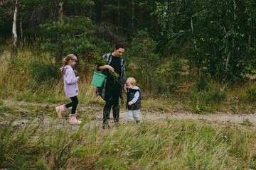 Fototapeta premium Happy family on a walk in the forest picking berries and herbs, traveling along paths and stones mom dad and children