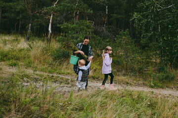 Fototapeta premium Happy family on a walk in the forest picking berries and herbs, traveling along paths and stones mom dad and children