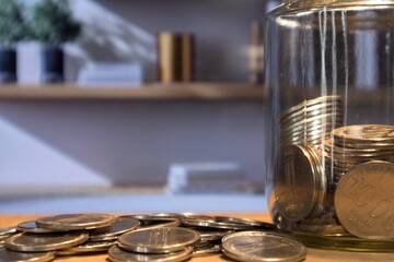Indonesian Rupiah coins in glass jar and scattered coins on wooden table in living room