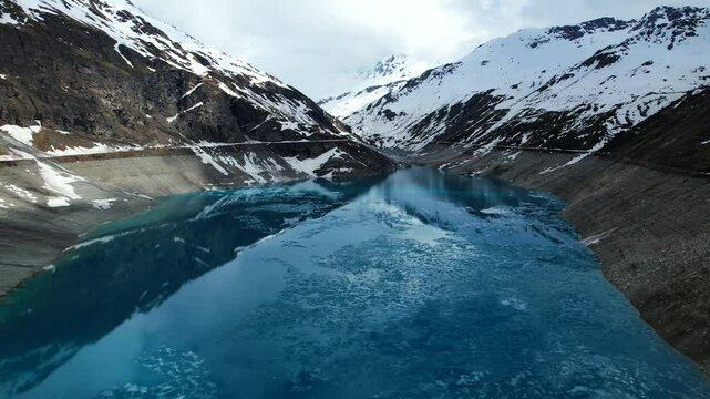 4k Drone Aerial Shot Of Vibrant Blue Glacial Water Of Lac de Moiry Dam Surrounded By Massive Snow Covered Mountains Reflecting On lake In Grimentz Switzerland