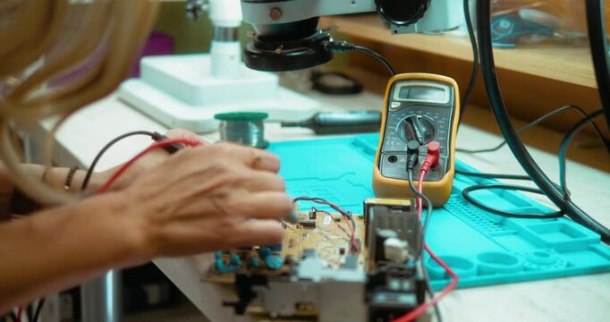 Female electrician engineer work tester measuring voltage and current of power electric on motherboard while working in electronics and computer service
