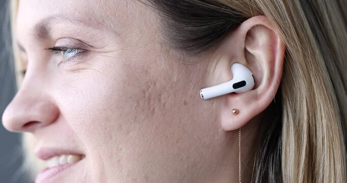 Smiling woman presses answer button on headphones in ear. Wireless trendy headphones concept