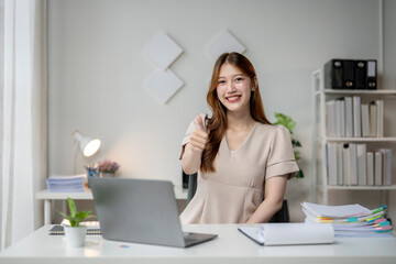 A woman is sitting at a desk with a laptop and a stack of papers