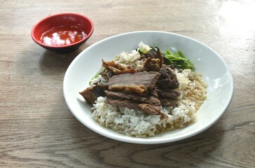 braised  slice cow leg stew black Chinese herb soup eat couple boiled Chinese kale on plain rice in plate dipping spicy sour chili sauce