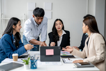 A group of people are sitting around a table, with a man pointing at a laptop