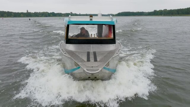 blond girl driving silver aluminum boat over river with trees on riverbank filmed with drone close up from front
