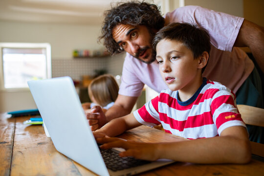 Father helping son with online learning on laptop at home
