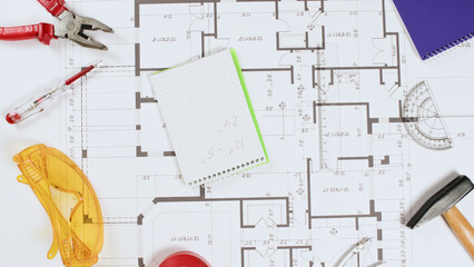 A notebook with notes and numbers lies on the drawing of the apartment, tools are laid out on the drawing