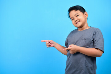 Beautiful asian young boy over isolated blue background smiling, showing and pointing something that is on his fingers. Copy space