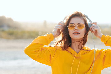 Stylish woman in yellow sweater and sunglasses listening to music on headphones outdoors