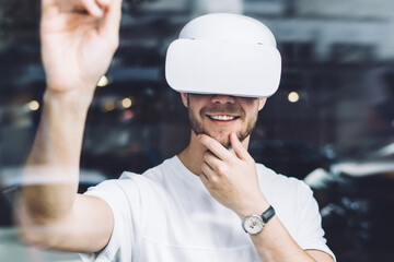 Happy man extends hand with digital stylus for interactive touch while standing indoors and using...