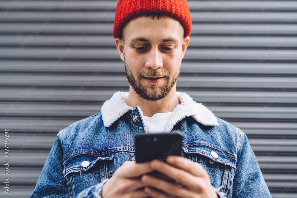 Poster handsome male blogger checking public comments in social networks while standing at urban setting wi