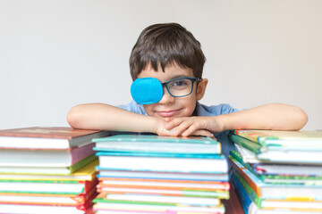 Happy cute boy in glasses and occluder with many books enjoys learning isolated on white background. Eye patch, amblyopia, strabismus. Learning concept