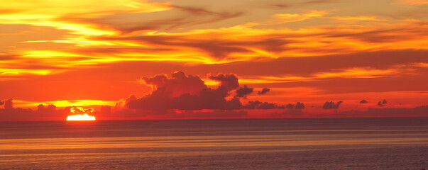 Vibrant sunset over calm ocean waters with dramatic clouds on the horizon