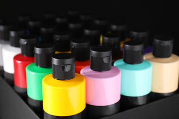 Acrylic paints of different colors in bottles against black background, closeup
