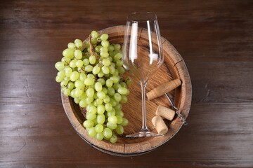 Corkscrew, glass, corks, grapes and wooden barrel on table, top view