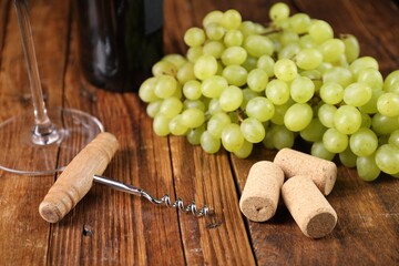 Corkscrew, corks and grapes on wooden table, closeup