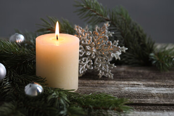 Burning candle, baubles and fir tree branches on wooden table, closeup. Space for text