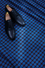 Male black leather shoes on dark blue checkered suit fabric background. Copy space for logo, design, advertising. Classic formal accessories for men