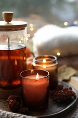 Burning candles, freshly brewed tea and autumn decor on fabric, closeup