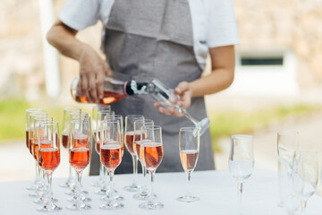 A waiter pours wine into glasses at outdoor buffet on white table.