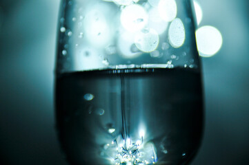 A glass filled with water, shades of blue, white bokeh from lights in the background