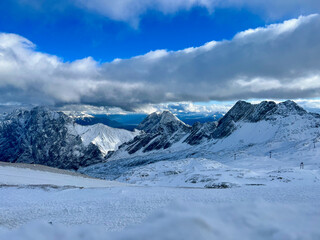 A stunning view of the snowy Alps from the top of Zugspitze in Bavaria, Germany. Snowy peaks stretch across the horizon, offering a majestic and serene alpine panorama.