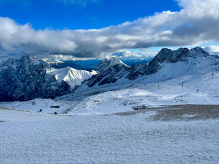 A stunning view of the snowy Alps from the top of Zugspitze in Bavaria, Germany. Snowy peaks stretch across the horizon, offering a majestic and serene alpine panorama.