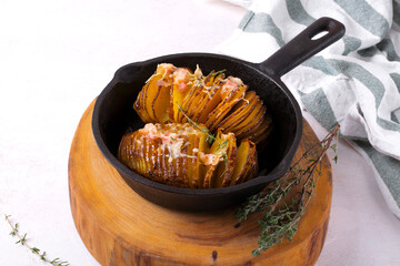 Hasselback potato roasted with cheese, bacon and aromatic herbs served in cast iron skillet. Hot...
