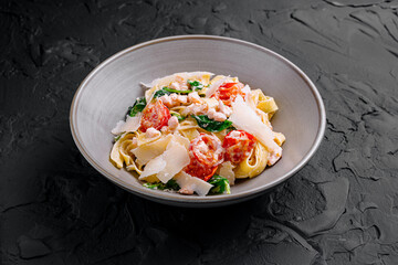 Pasta fettuccine with shrimps, spinach, cherry tomatoes and parmesan cheese on black background