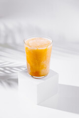 Refreshing mango smoothie standing on white cube with tropical palm leaf shadow
