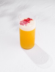 Refreshing yellow cocktail with white foam and raspberry powder topping on white background