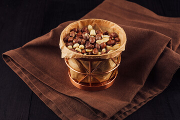 Copper basket overflowing with roasted peanuts sitting on brown napkin