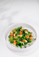 Fresh and healthy salad with salmon, avocado and spinach, served on a white plate