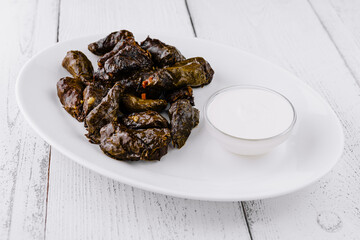 Serving plate presenting stuffed grape leaves dolma with yogurt dip on rustic white table