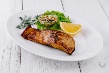 Grilled salmon fillet served on a white plate with lemon and sauce
