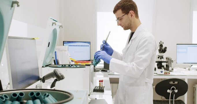 Male doctor places the blood tests in the centrifuge. From above centrifuge machine with test tubes spinning then stopping during workday in modern lab. Centrifuge machine with vials in laboratory.