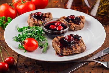 Grilled beef medallions with cherry sauce on white plate