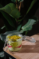 Delicious pistachio dessert with red fruit jelly in a glass jar standing on wooden table
