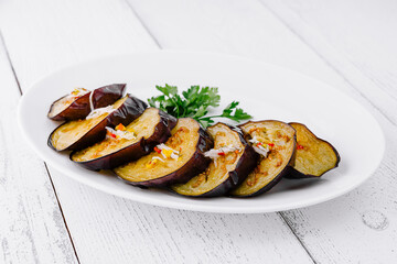 Slices of grilled eggplant with garlic and herbs on white plate