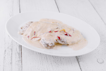 Meat with white sauce and red pepper on white plate