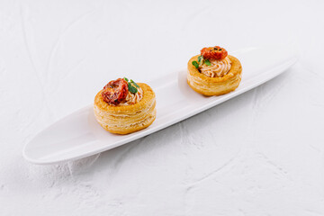 Delicious vol-au-vents with salmon, cream cheese and sun-dried tomatoes, garnished with herbs on white background