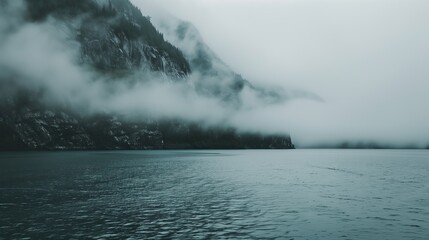 Naklejka premium misty mountainside looms over calm waters