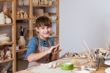 teenager boy works with clay makes  ceramic plate in pottery school.  Children arts a crafts class in workshop. child sculpts from clay